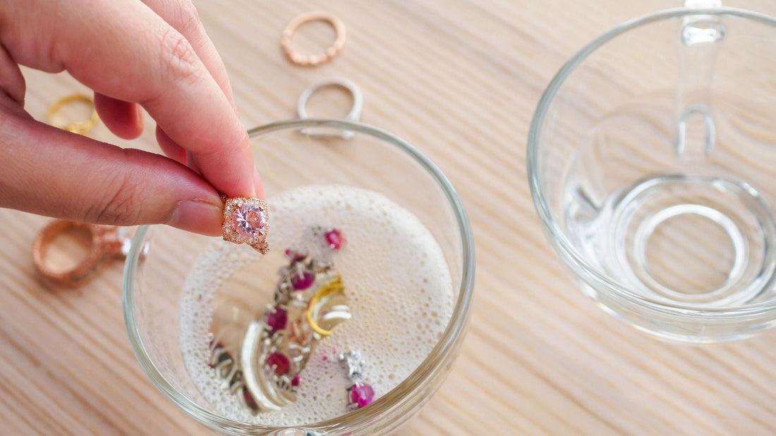 Jewellry in a clear glass bowl with soap water, and a hand holding a ring