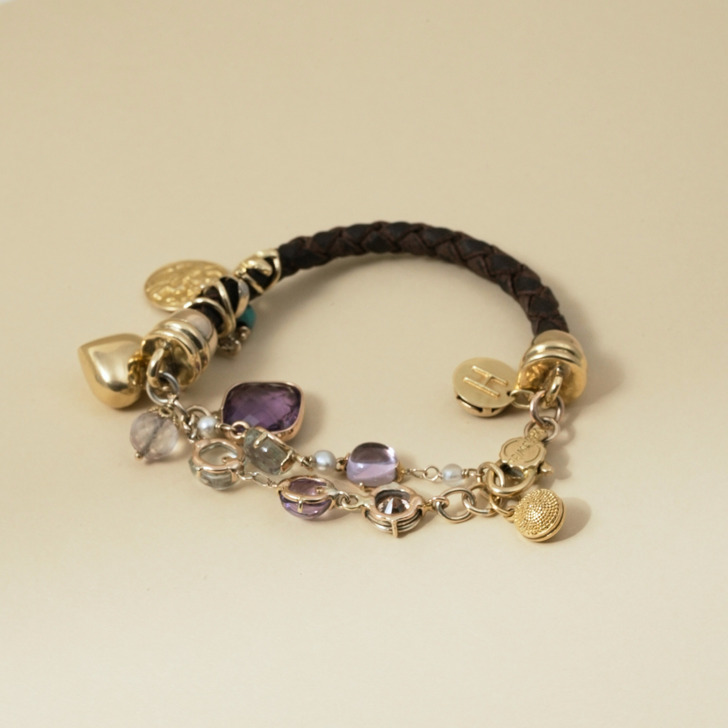 A whimsical charm bracelet featuring braided leather, vibrant gemstones, and sculptural gold details. Rich with texture, colour, and charm.